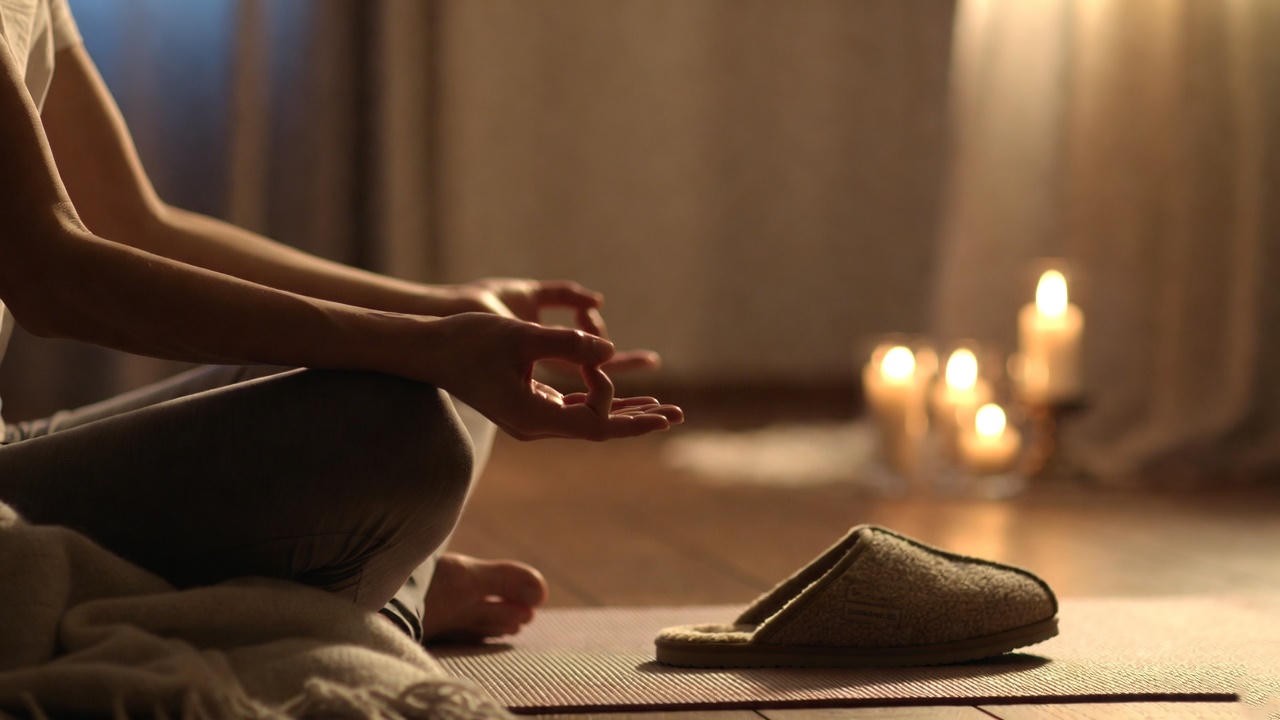 Person in Barefoot Dreams slippers practicing meditation during cozy evening wind-down routine for better sleep.