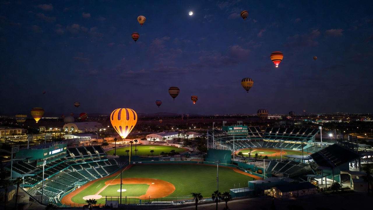 Nighttime view of Big League Dreams Cathedral City replica baseball fields with hot air balloons glowing in the sky.
